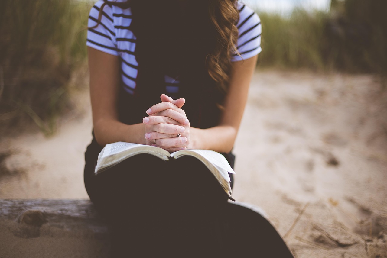 A woman with her hands clasped in prayer over an open Bible, symbolizing deep study and reflection.